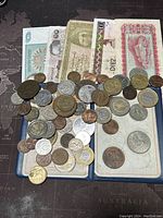 Coins in various metals and sizes laid over banknotes featuring different designs and currencies, shown on a map background.