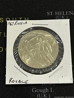 Obverse side of 1967 USSR 1 Rouble coin showing Lenin and Soviet symbols encased in white cardboard holder.