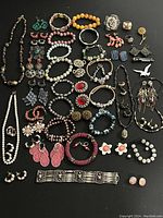 Full view of assorted colorful jewelry laid out on black background including necklaces, bracelets, earrings, pins, and rings.