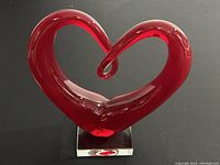 Front view of red glass heart sculpture on a clear base, showing shape and color details.