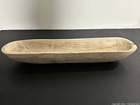 Side angled view of a large wooden elongated bowl with visible wood grain and smooth unfinished surface.