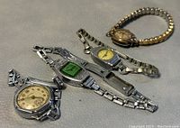Four ladies vintage mechanical wristwatches laid on a grey surface, showing faces and bands.