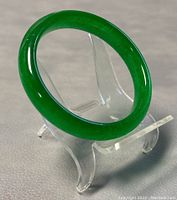 Green polished jade bangle shown upright on clear stand, highlighting the band thickness and smooth glossy finish.