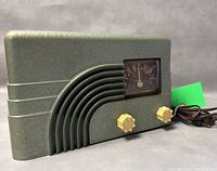 Front angle view of green vintage Northern Electric Baby Champ Deluxe radio showing tuning knobs and dial.
