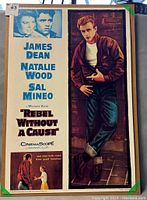 Front view of reproduction film poster showing cast names, film title, and image of James Dean leaning against a brick wall.