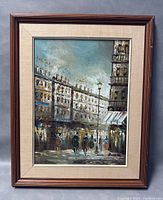Full view of framed oil painting depicting a rainy European style street scene with figures walking and lit buildings.