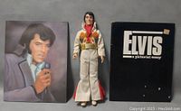 Photo of vintage Elvis Presley doll standing between two Elvis pictorial essay books, showing front views of all items.