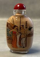 Front view of the snuff bottle showing a man and woman in traditional attire with interior elements and calligraphy.