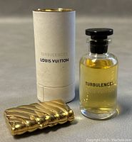 Mini Louis Vuitton Turbulences Eau de Parfum bottle next to gold-toned compact and white tubular packaging.