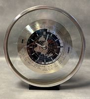 Front view of vintage round world GMT clock showing the world map, hour markers, and city/time zone names.