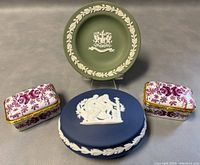 Front view of all items in the lot: green jasperware plate standing, blue jasperware box, and two purple floral porcelain trinket boxes