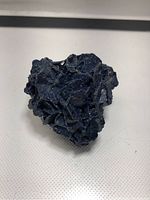Front view of a natural dark blue azurite mineral cluster with detailed crystal structure on a white surface.