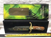 Collector hunting cutting utensil displayed inside original presentation box, showing full length of knife with brass guard and deer design on blade and handle.