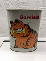Front side of metal garbage can with large Garfield image and text.