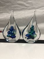 Pair of clear blown glass sculptures with aqua blue and green internal swirl designs, teardrop shape with flat base, shown front view.