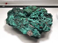 Photo showing top and angle view of large natural rough green malachite crystal quartz specimen with diverse textures including botryoidal areas and rough mineral matrix.