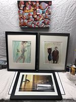 Overview of the 4 picture frames arranged on the floor; includes three with black frames and mounted artworks, one colorful crowded animal painting on top