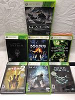 Seven Xbox 360 game cases displayed showing front covers with titles: Halo Anniversary, Skyrim, Mass Effect 2, Command and Conquer 3, Left 4 Dead 2, Halo 4, Dead Space 2.