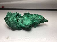 Photo showing natural green raw malachite stone from side angle revealing rough texture and mineral structure.
