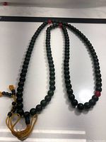 Full length of Tibetan praying mala showing 108 dark greenish-black beads with spaced red beads and yellow tassel.