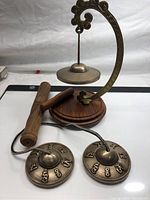Full display of all items showing Tingsha cymbals, bell with curved metal arm, wooden base and striker.