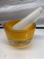 Yellow glass mortar holding a white glass pestle, showing the thickness and color of the mortar glass and the pestle's shape.