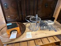 Photo of a glass ice bucket with metal band and clip tongs, a wooden box with dark stone top, and a metal bar strainer on a wooden surface.
