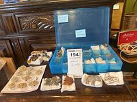 Wide view of ladies costume jewelry laid out on a wooden dresser and inside a segmented plastic container. Includes various brooches and pins in multiple designs.