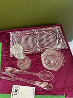 Photo showing the entire crystal set including tray, bottle with stopper, bowl, and serving utensils on a maroon quilted surface.