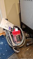 Dyson DC32 vacuum cleaner, showing the red cyclonic bin, attached hose coiled around the vacuum base, and a gray wand attachment leaning against it. Operating manual is also visible.