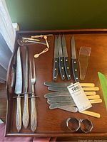 Overview of the entire lot showing knives, forks, spoons, and napkin rings on a wooden tray.