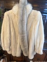 White fur ladies jacket hanging with soft, fluffy texture and shawl collar.