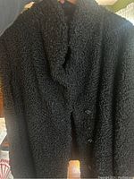 Photo showing close-up of black lambs wool jacket with curly textured wool fabric, front including buttons and collar visible