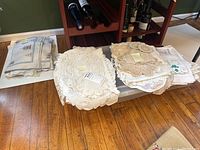 Photo showing stacks of smaller lace items and linens laid out on a table including rectangular pieces with scalloped edges and doilies.