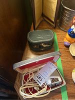 Green leather zippered travel tie keeper case on wooden surface next to the shaver box.