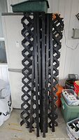 Photo of stacked wooden trellis panels and tracking pieces leaning against a cabinet showing lattice design and painted black finish
