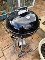 Photo of the Weber black charcoal kettle grill with domed lid and thermometer on a stone patio.