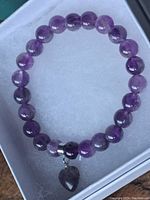 Top-down image showing the amethyst beaded bracelet arranged in circle with its heart-shaped charm centered.