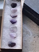 Photo showing seven amethyst carved heart stones arranged in a row inside a box with cushion lining.