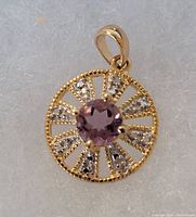 Front view of circular gold plated sterling silver pendant with light purple round amethyst center stone and clear accent stones arranged in a spoke-like pattern.