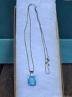 Full view of the blue topaz pendant necklace laid flat inside a presentation box, showing the pendant and chain.