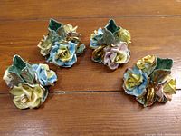 Set of four Capodimonte floral ceramic candle holders with multicolored rose flowers and green leaves, shown on wooden floor.