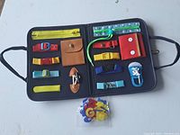 Open navy blue learning skill tote showing multiple fastening activities including zipper, buckles, buttoned flap, snap buttons, shoelace, and velcro strips with a separate pack of foam velcro letters.