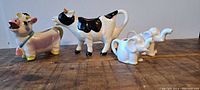 Four ceramic creamers: two cow-shaped and two elephant-shaped on wooden surface