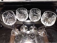 Four crystal wine glasses shown in a row with light etched patterns and clear stems.