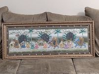 Full view of framed painting on cloth depicting elephants and attendants in a parade scene, resting on couch for scale.