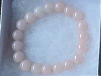 Close-up of the round light pink rose quartz beads forming a stretch bracelet shown in a white box with a soft white cushion inside.