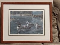 Framed and matted print showing the full artwork with wooden frame and glass, featuring three loons in a lake scene.