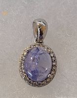 Front view of the tanzanite pendant showing the oval blue tanzanite cabochon surrounded by cubic zirconia stones in a silver setting.