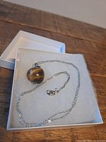 Sterling silver chain with tigers eye apple pendant in a white jewelry box.